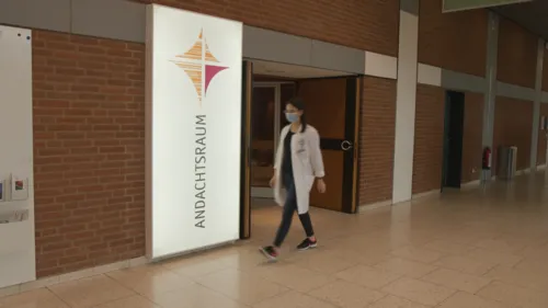 Eine Frau auf dem Flur eines Krankenhauses vor der Eingangstür zu einem Andachtsraum.